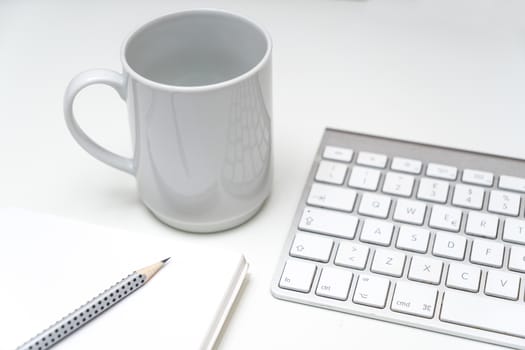 a cup of coffee on the desk, between a keyboard and a clipboard