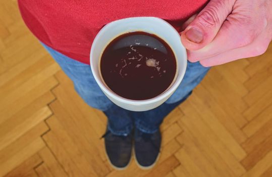 Man is holding morning cup of coffee. Man with cup of coffee standing on  parquet floor. Close-up. Copy space.