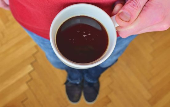 Close up of man hand holding cup of coffee. Man is holding morning cup of coffee. Man with cup of coffee standing on  parquet floor. Close-up. Copy space. Retro colors. 