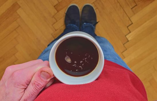 Man is holding morning cup of coffee. Man with cup of coffee standing on  parquet floor. Close-up. Copy space.