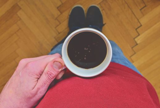 Man is holding morning cup of coffee. Man with cup of coffee standing on  parquet floor. Close-up. Copy space.