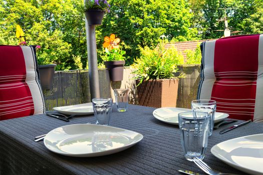 Covered balcony table with white plates, drinking glasses and dining table with two chairs with modern seat covers.