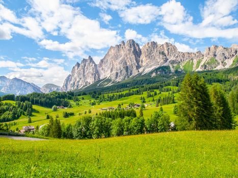 Rocky ridge of Pomagagnon Mountain above Cortina d'Ampezzo with green meadows and blue sky with white summer clouds, Dolomites,, Italy.