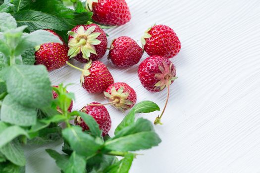 Red strawberries with green herbal mix of fresh mint and melissa herbs on white wooden background