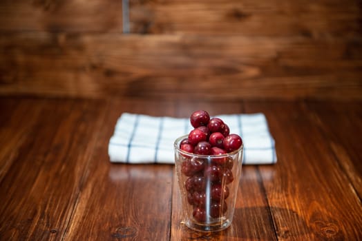 Sweet cherry, black cherries in a glass on wooden background.