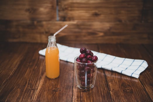 Sweet cherry, black cherries in a glass on wooden background with fresh juicy in glass bottle.