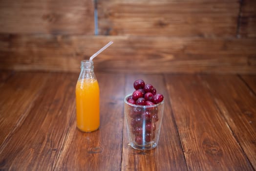 Sweet cherry, black cherries in a glass on wooden background with fresh juicy in glass bottle.