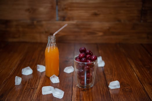 Sweet cherry, black cherries in a glass on wooden background with fresh juicy in glass bottle. Ice around