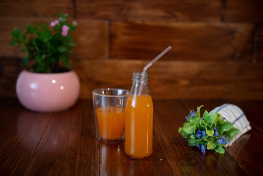 Fresh juice in bottle on wooden table with flowers