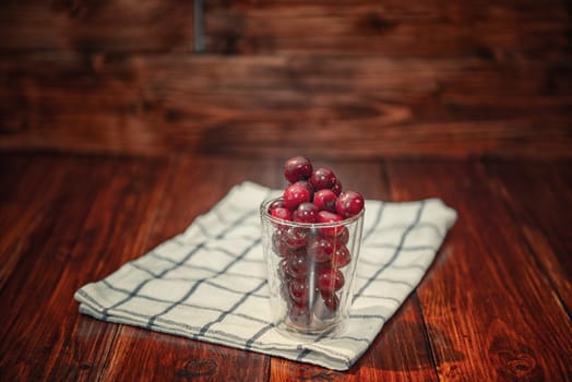 Sweet cherry ( black cherries) in a glass on wooden background.