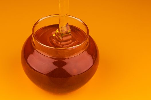 Pouring honey in glass pot isolated on yellow background