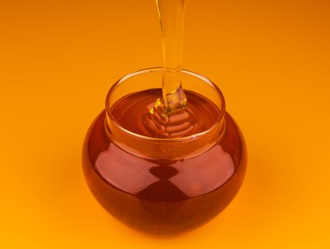 Pouring honey in glass pot isolated on yellow background