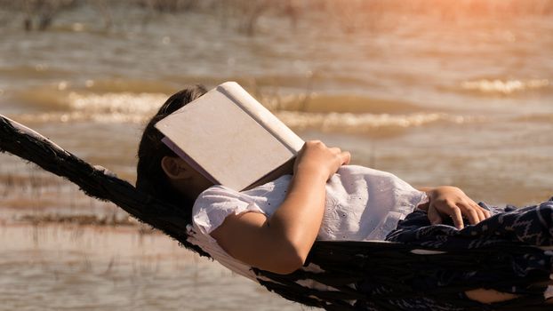 Close up of young beautiful girl sleeping in a hammock and holding a book with her hands