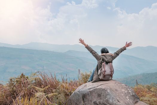 Hipster girl with backpack sitting in a rocky top of the mountain against the blue of sky