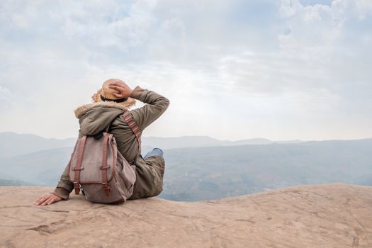 Hipster girl with backpack sitting in a rocky top of the mountain against the blue of sky