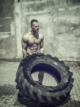 Handsome muscular young man exercising, flipping big tire outdoor