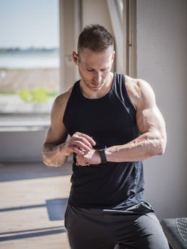 Young attractive man in gym checking sports watch to track his workout, heart pulse or fitness