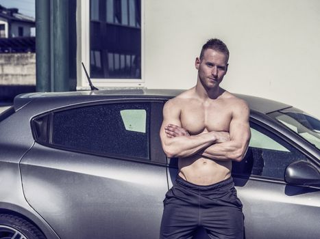 Portrait of young blond handsome muscular topless man leaning on car