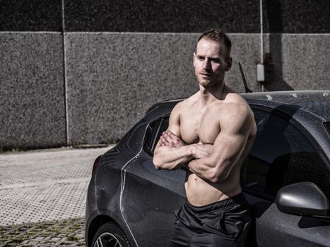 Portrait of young blond handsome muscular topless man leaning on car