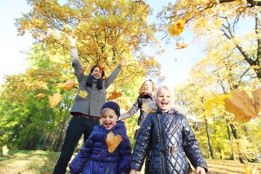 Happy family playing with autumn maple leaves in park