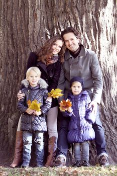 Happy family in autumn park near big tree trunk