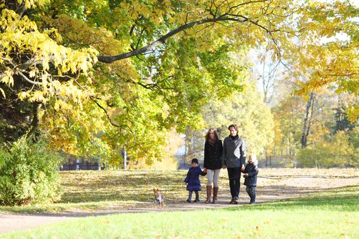 Happy family with two children walking in autumn park holding hands