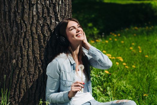 Young brunette woman with headphones listening to the music in park on sunny summer day