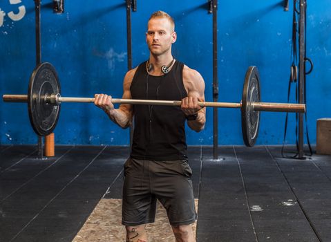 Handsome muscular young man exercising arms in gym with barbell.