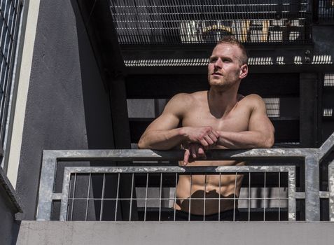 Portrait of a sexy muscular young man shirtless in urban environment, walking on metal stairs, looking away