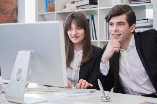 Business people working in the office, lookinf together at computer monitor and smiling