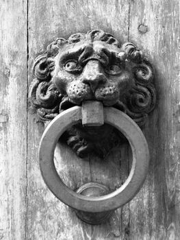 Vintage metal door knocker on old wooden door. Black and white image.