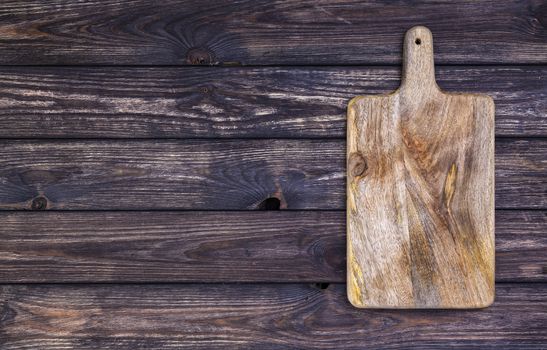 Cutting board on dark wooden table. Top view. Copy space