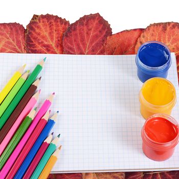 Colored pencils with notebook and autumn leaves