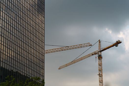 Industrial picture: high cranes in the high sky near the skyscraper made of metal and glass