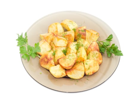 Serving of the country style fried potatoes sprinkled by chopped dill with twigs of parsley on the dark glass dish on a light background
