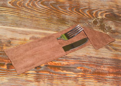 Fork and knife made of a stainless steel in the brown textile cutlery pouch on the old wooden table
