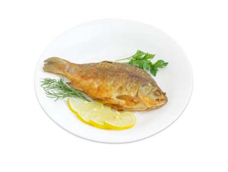 Fried crucian, slices of the lemon, twigs od the parsley and dill on a white dish on a white background
