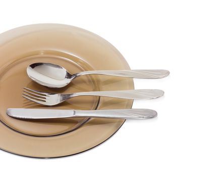 Fragment of the dark glass dish and eating utensils, consisting of spoon, fork and knife made from stainless steel on it closeup on a light background
