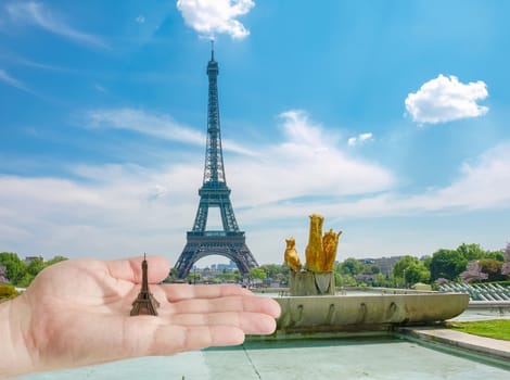 View of the Eiffel Tower from the Trocadero Square with small metal Eiffel Tower model on the man's palm in the foreground in Paris
