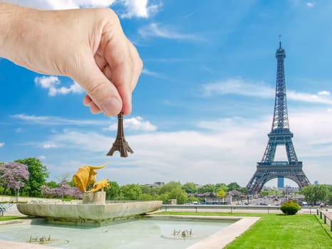 View of the Eiffel Tower from Trocadero Square with sculptures and small metal Eiffel Tower model in man's hand in a foreground in Paris
