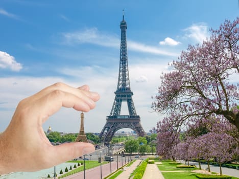 Eiffel Tower with with blossoming trees and small metal Eiffel Tower model in man's hand in a foreground in Paris
