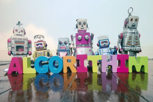 the word ALGORITHIM  with wooden letters and retro toy robots  on an old wooden floor with reflection