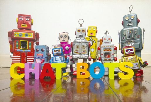the word A CHAT BOTS  with wooden letters and retro toy robots  on an old wooden floor with reflection