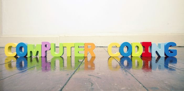 the words COMPUTER CODING  with wooden letters on an old wooden floor with reflection