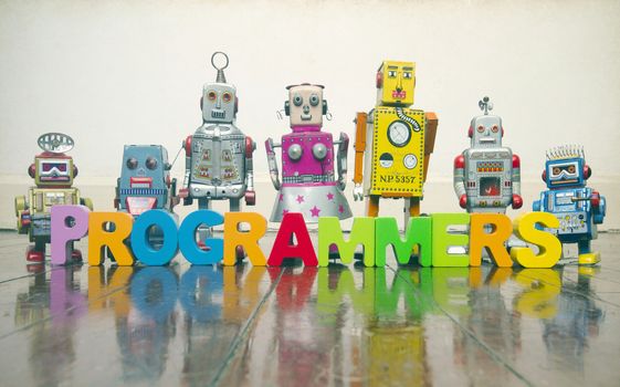 the word  PROGRAMMERS with wooden letters and retro toy robots  on an old wooden floor with reflection