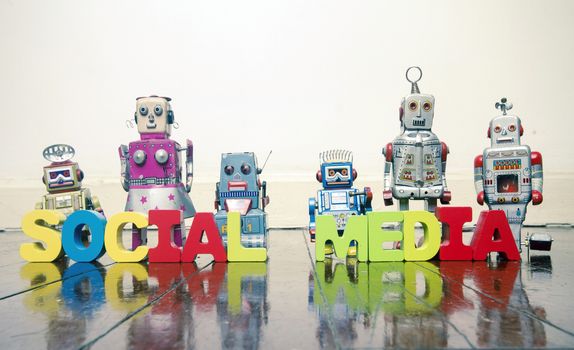 the words SOCIAL MEDIA   with rtro robot toys on a wooden floor with reflection