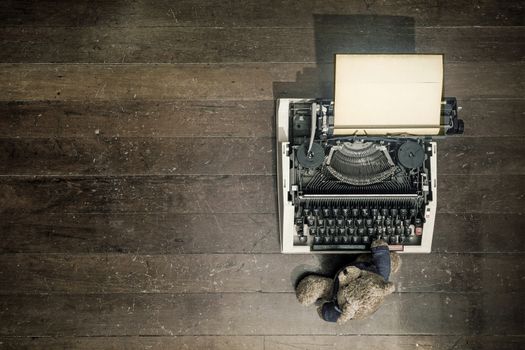 an old teddy bear at on a vintage typewriter from above  on a wooden floor 