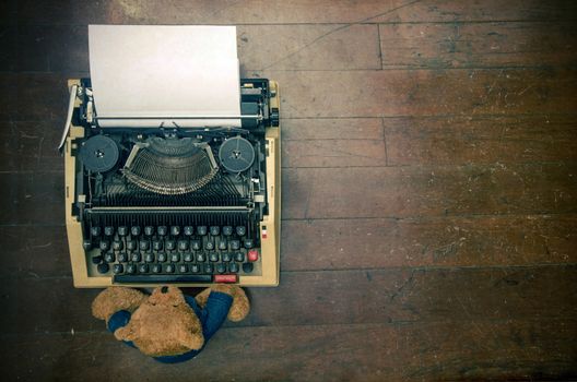 old teddy bear at a retro  typewriter  a wooden floor from above 