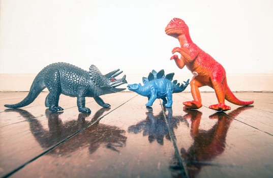 three  dinosaur toys on a old wooden flor with reflection