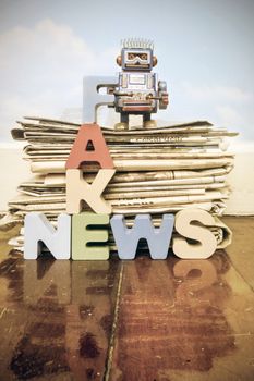 one retro robots  a pile of old newspaper with the word FAKE NEWS on a wooden floor